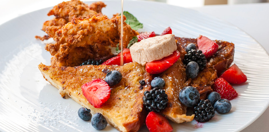 A closeup of a french toast topped with fruits and a fried protein