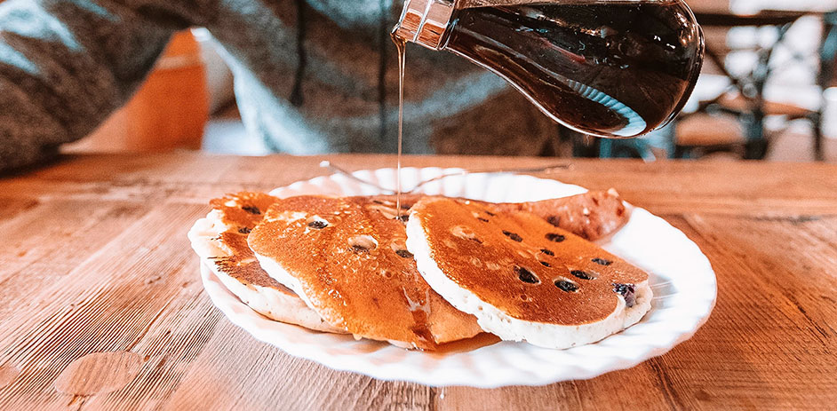 pouring maple syrup on chocolate chip pancakes