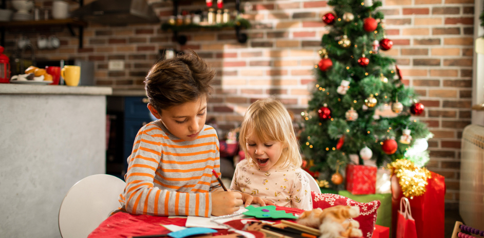 two children writing their christmas list in front of a christmas tree