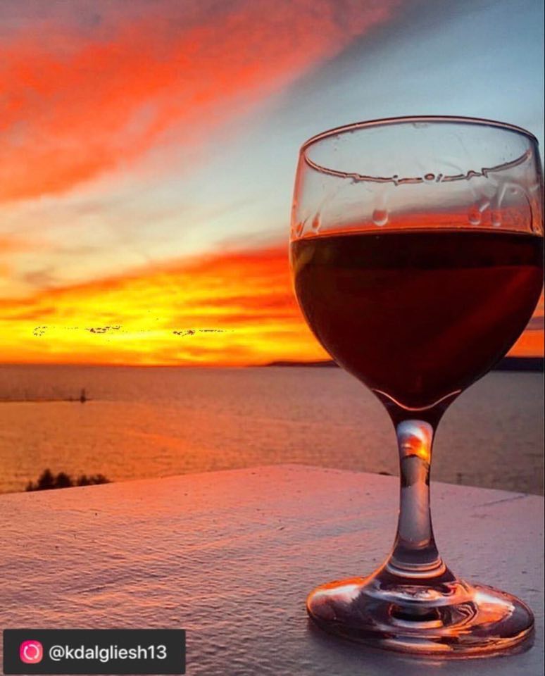 sunset with red, yellow, and blue sky with the ocean in the background and a glass of wine