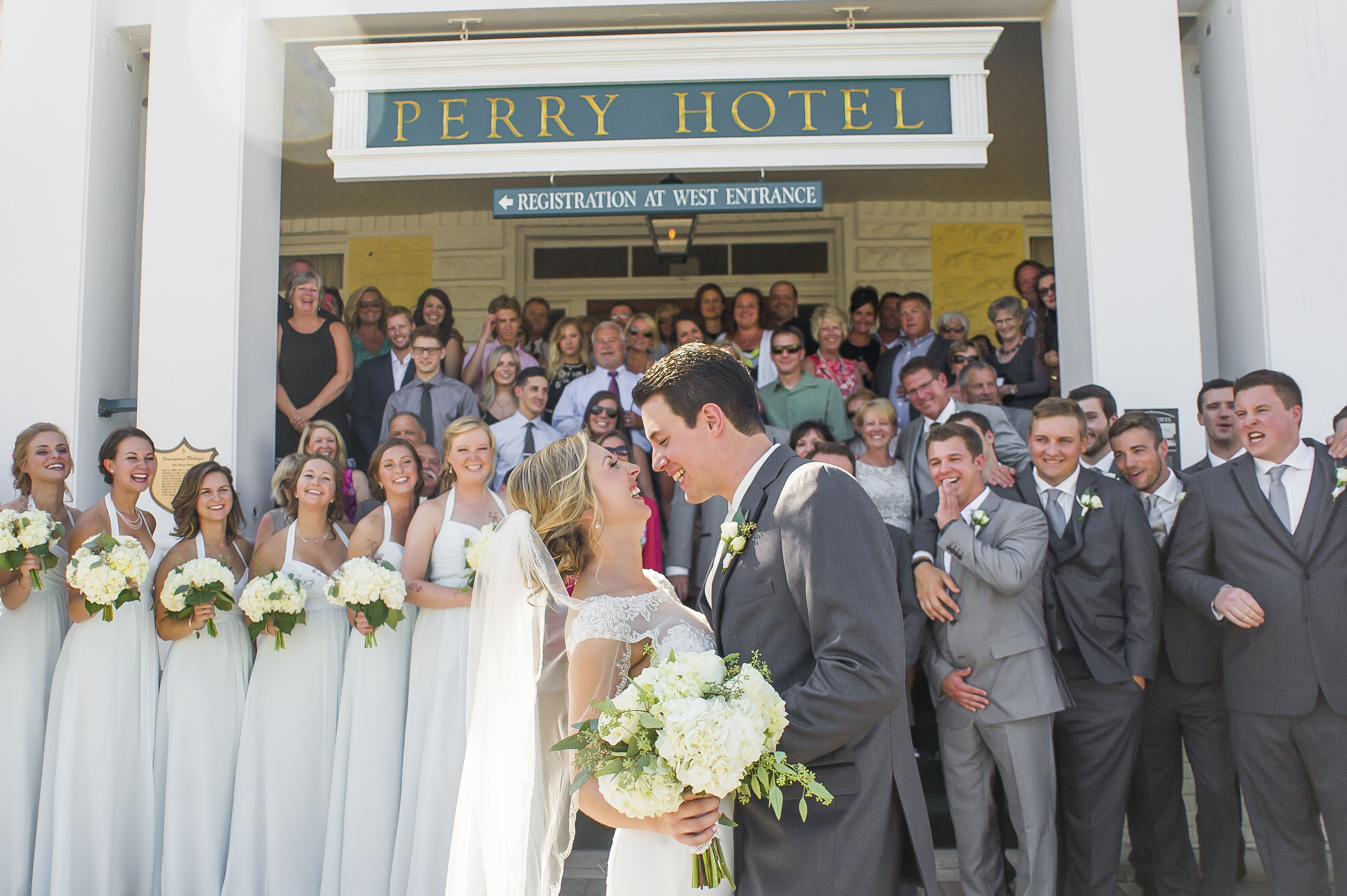 bride and groom smiling at each other with hotel and guest in the background