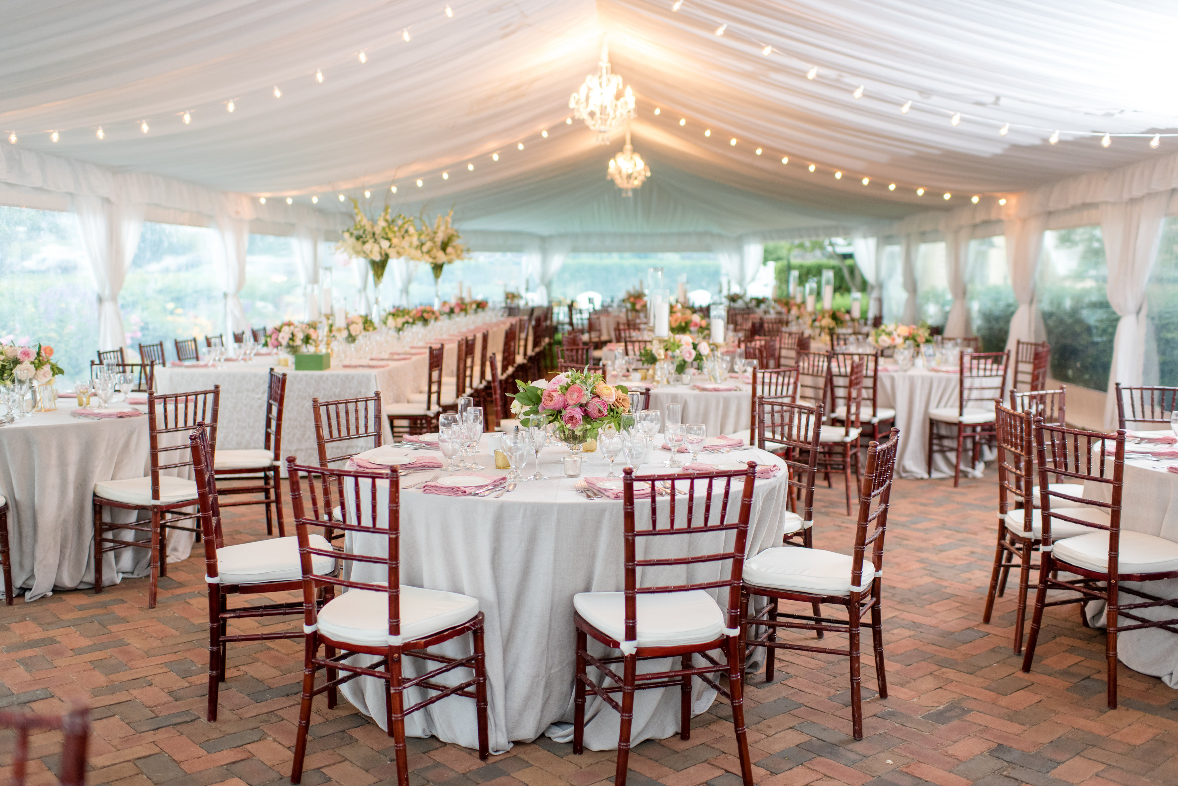 many sets of chairs and tables set up under large white tent with hanging lights