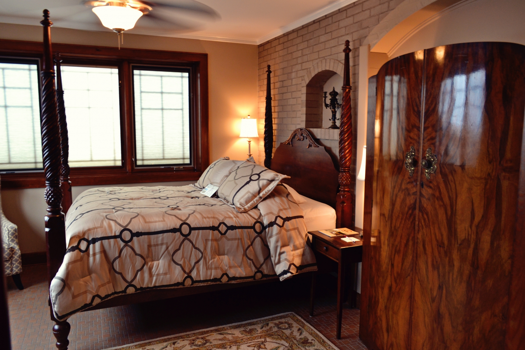 hotel room dark patterned bedding with wooden cabinet, brick wall, and large window 