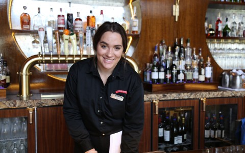 Woman in black uniform and dark hair working behind the bar