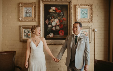 Bride and groom holding hands in venue with picture frames in the background 