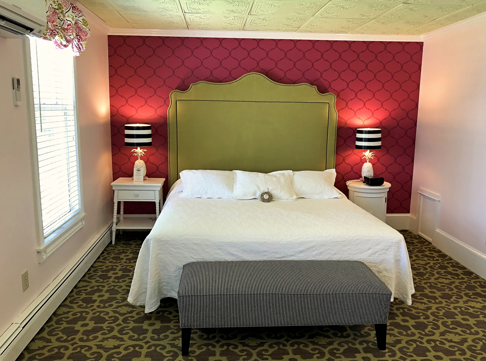 interior hotel room with red wallpaper and large green headboard and green carpet 