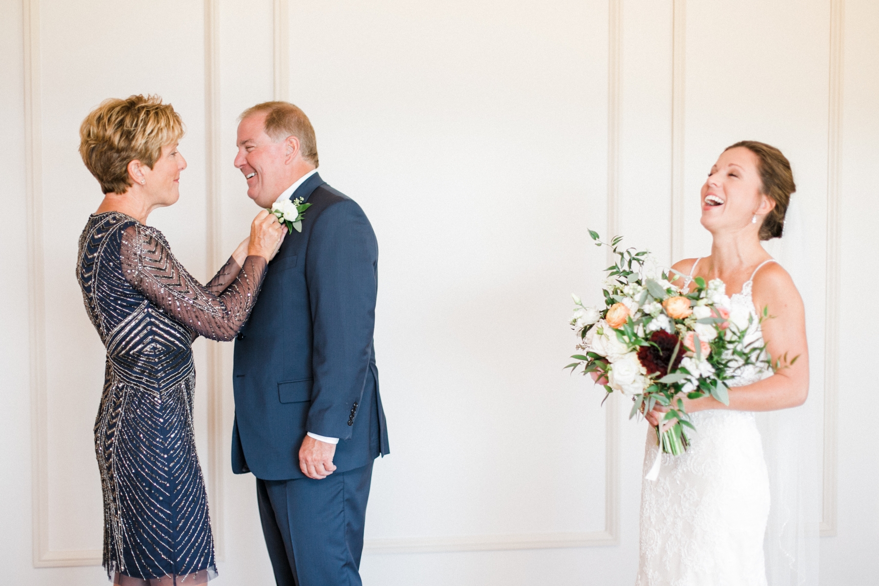 woman in blue beaded dress placing a flower on the mans coat with a bride laughing 