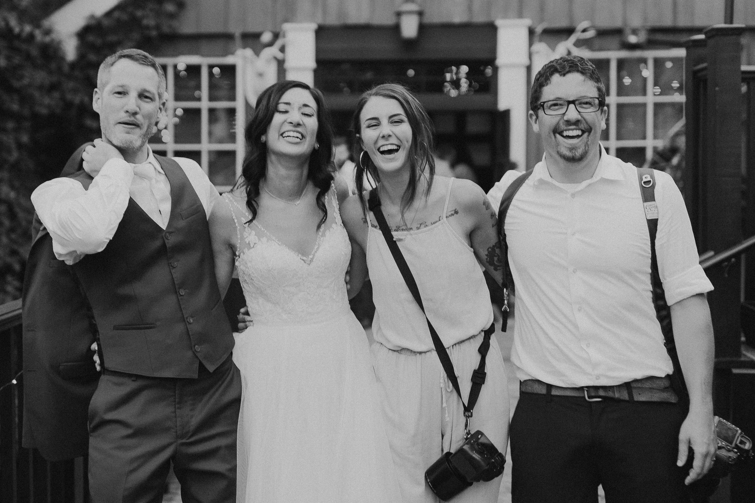 Black and white image of bride and groom smiling with the photographers 