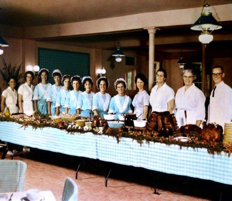 older picture of the staff ready to serve guest behind a buffet table 