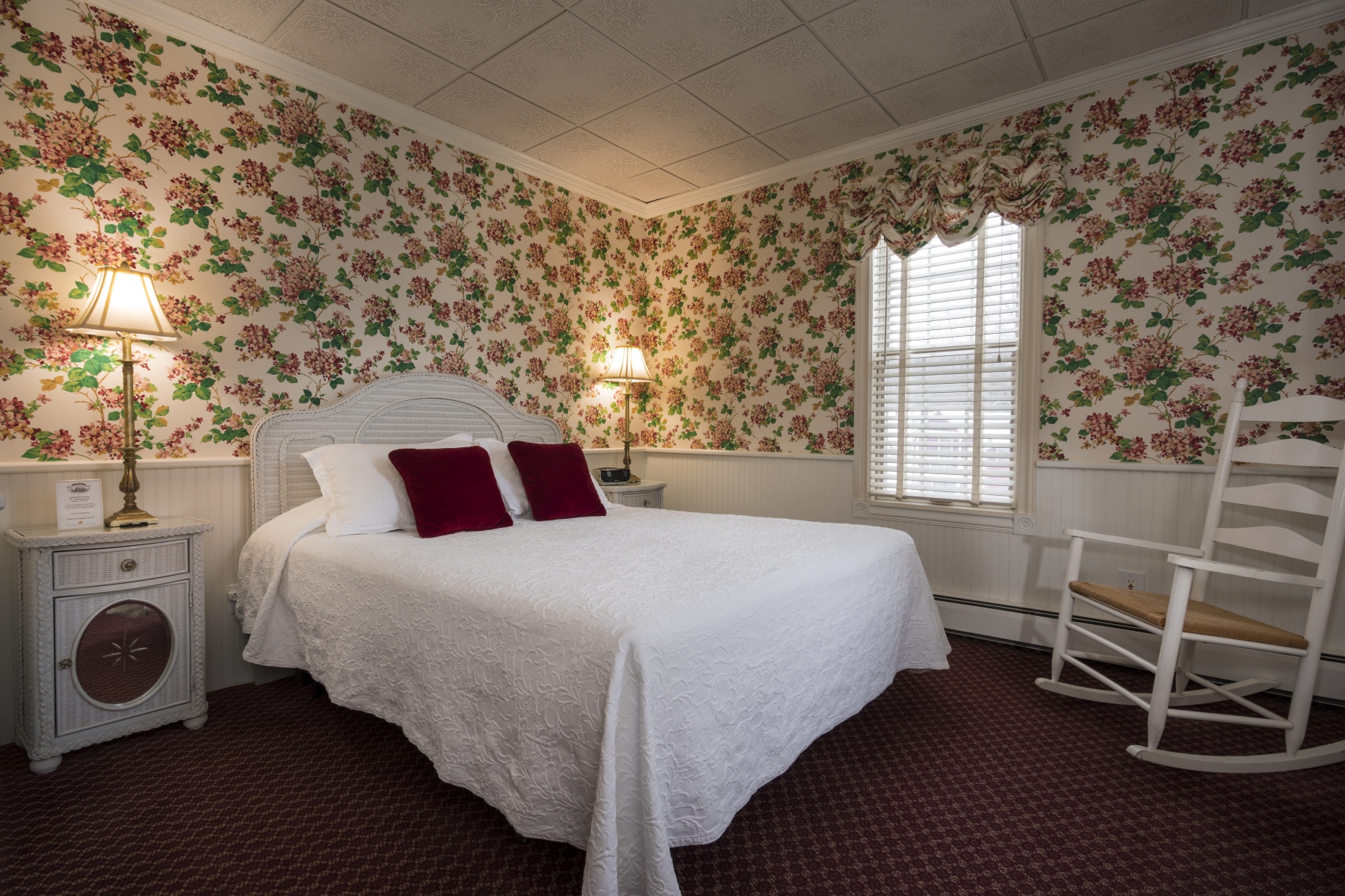 hotel room with floral wallpaper and large bed with white pillows and sheets 