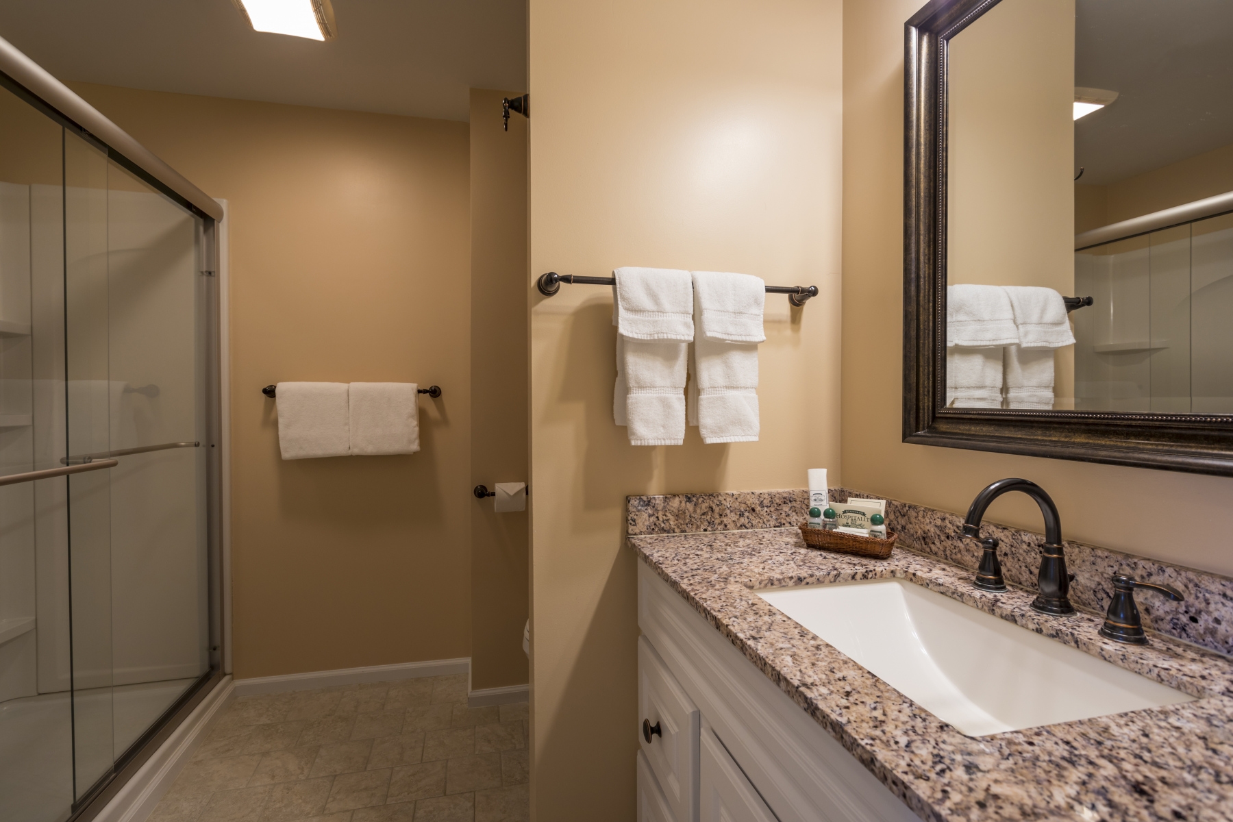 hotel bathroom with walk in shower, granite counter tops and large mirror 