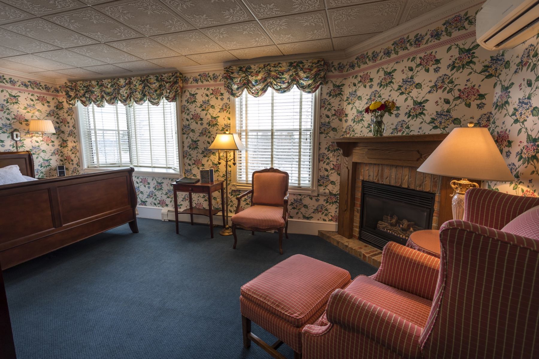 large hotel room with floral wallpaper and red chairs next to the bed and fireplace 