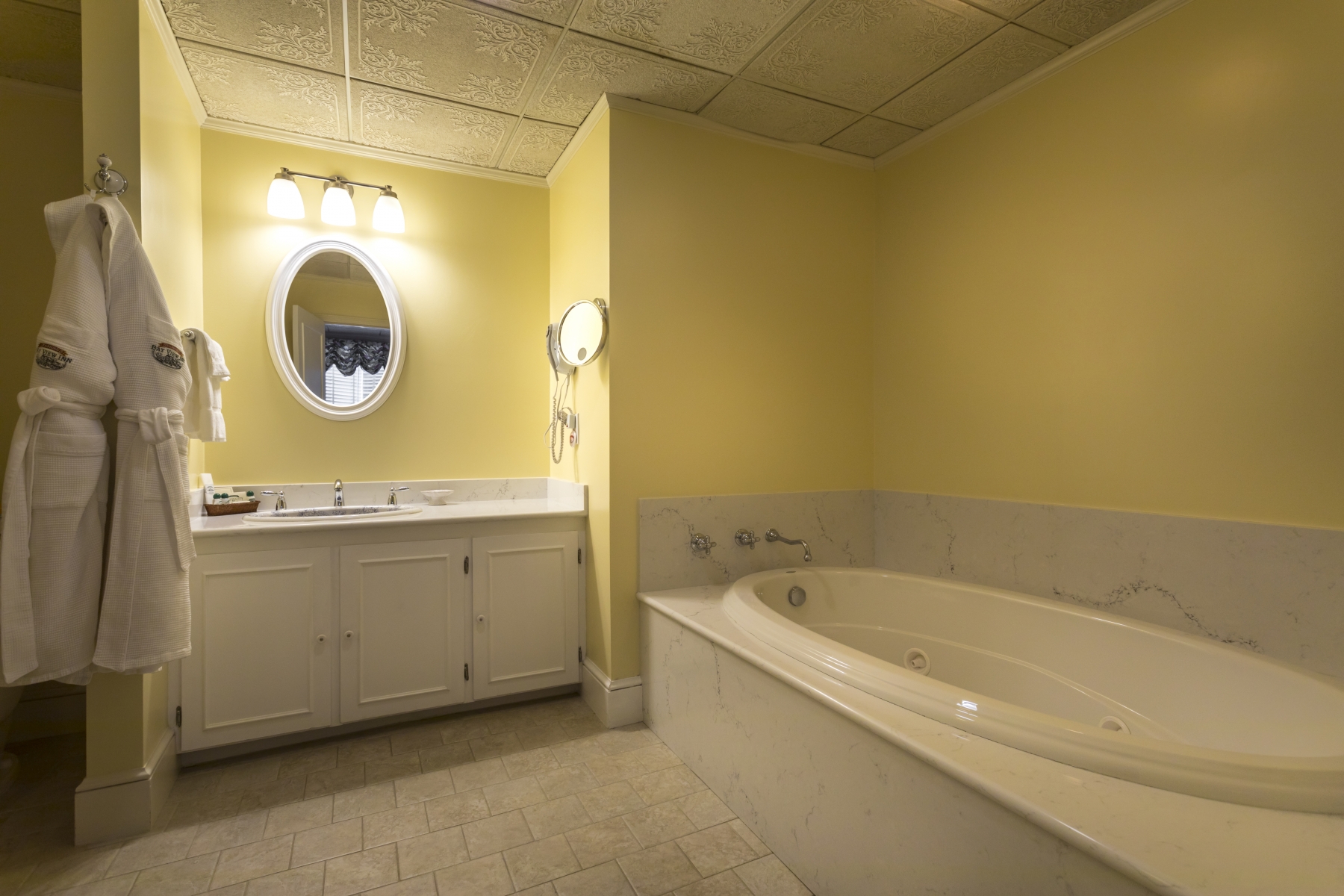 hotel room bathroom with granite counter tops and yellow wall and large tub