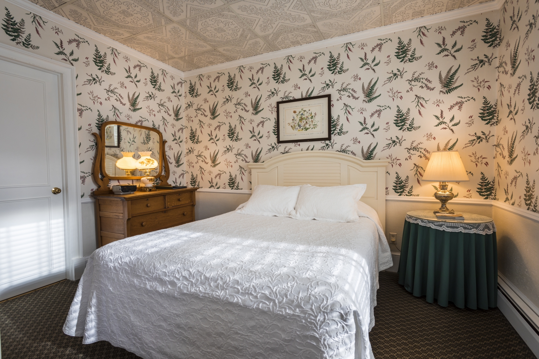 large hotel room with floral wallpaper white bedding and a night stand with a lamp 
