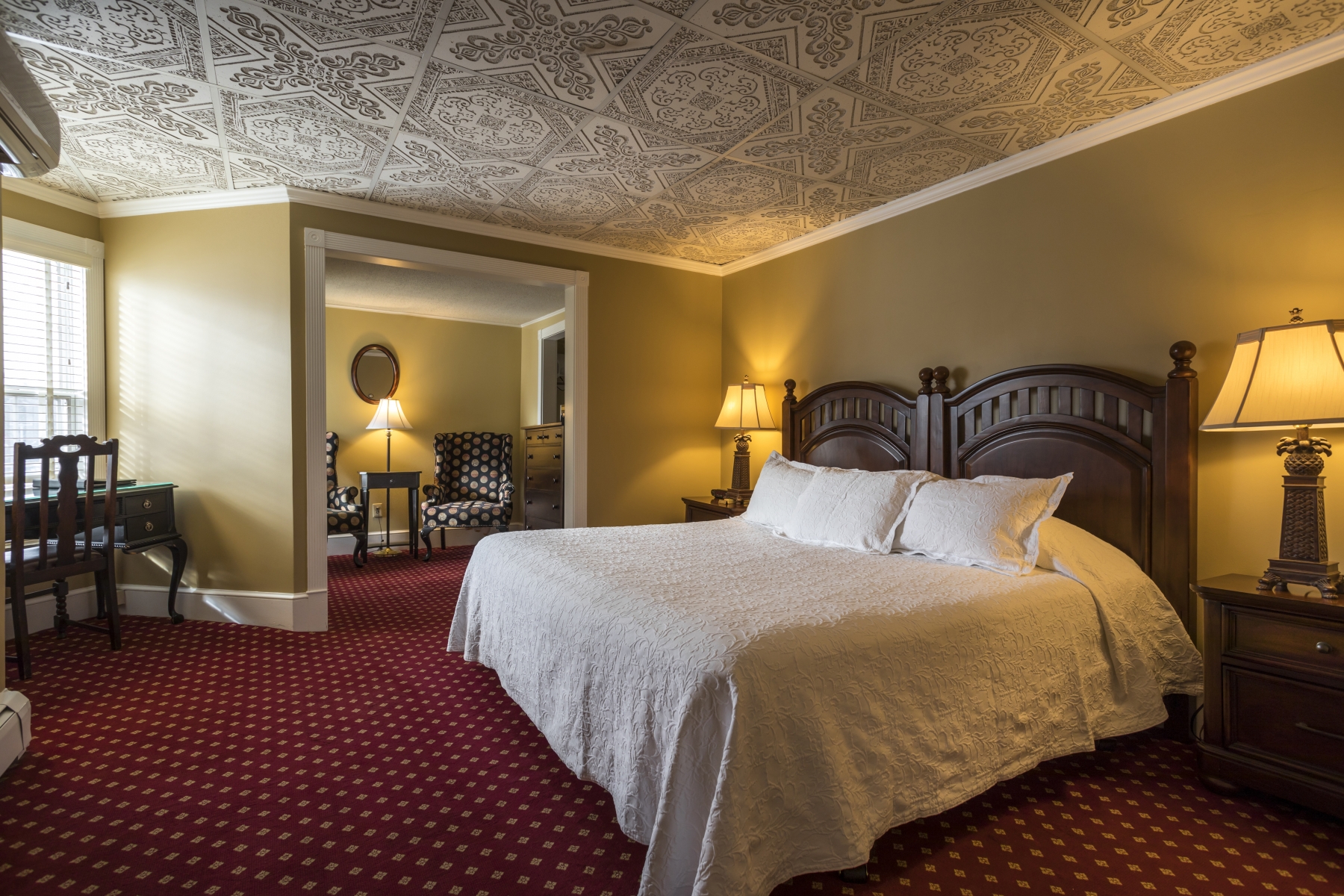 large hotel room with red carpet white bedding and patterned wallpaper on the roof