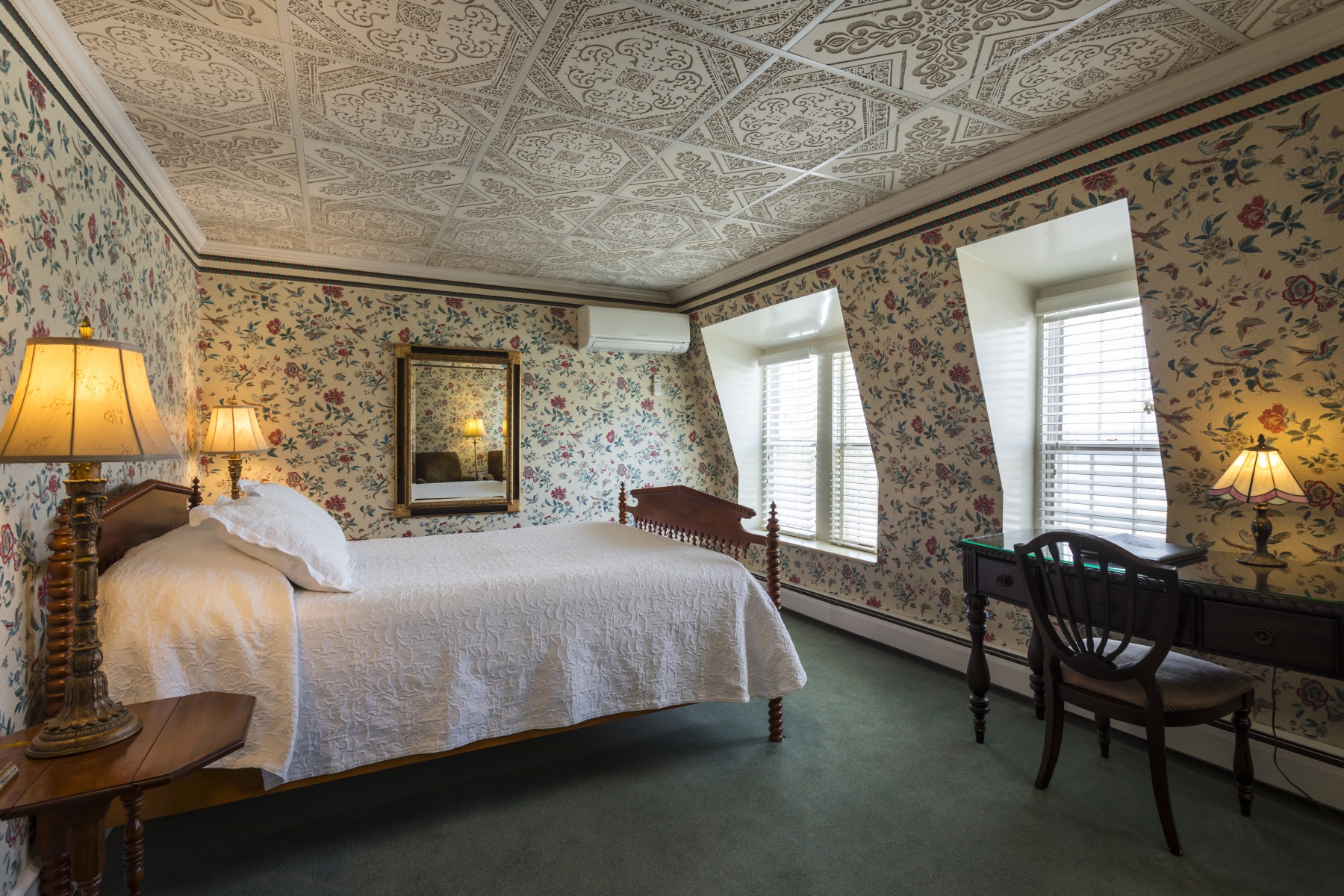 large hotel room with floral wallpaper white bedding and two windows