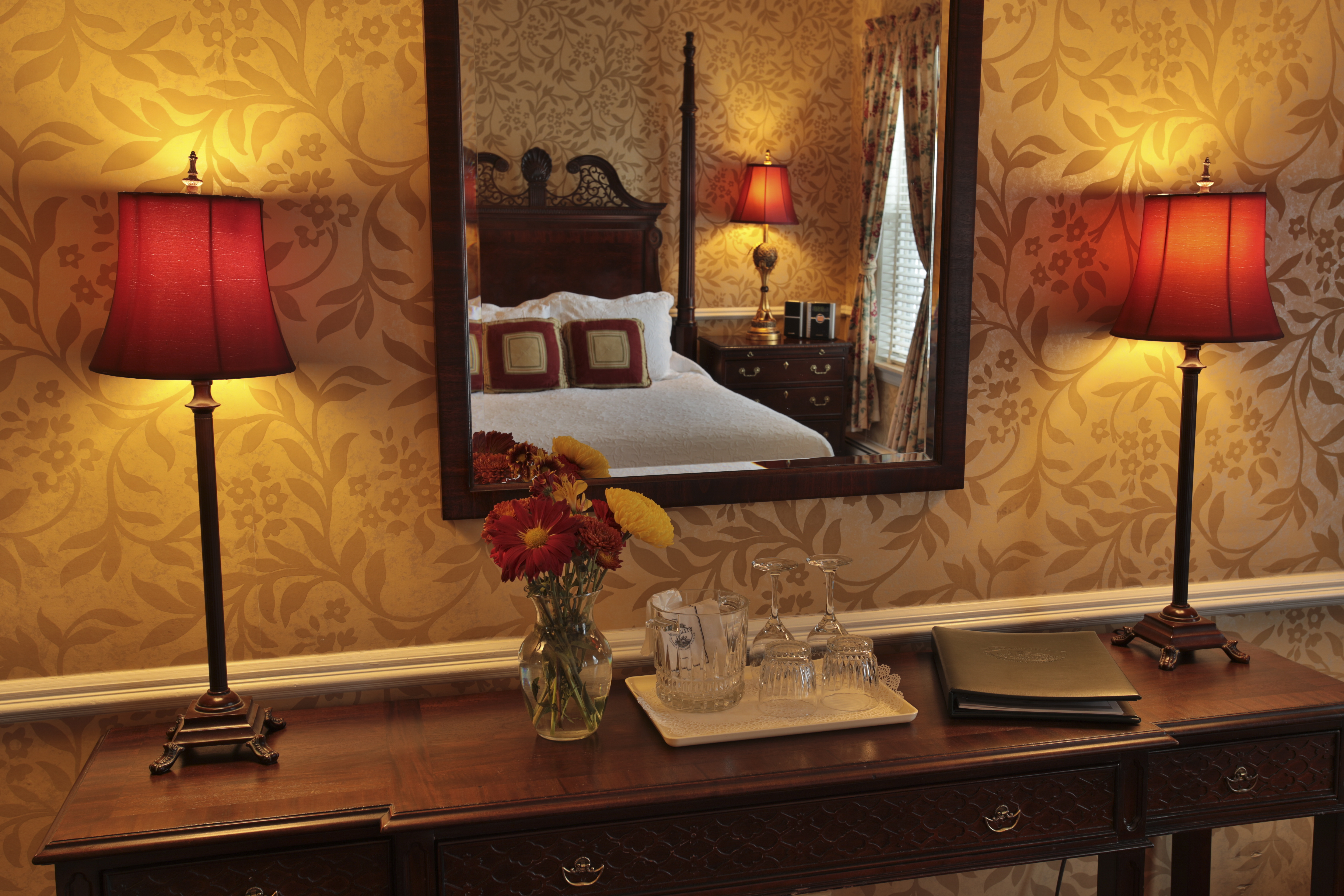 desk in hotel room with two red lamps and tan floral wallpaper