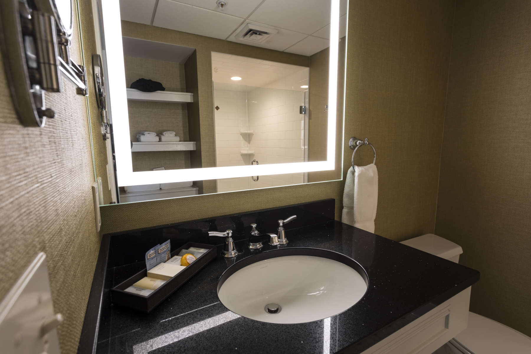 bathroom mirror with lights on around the edge and black counter top