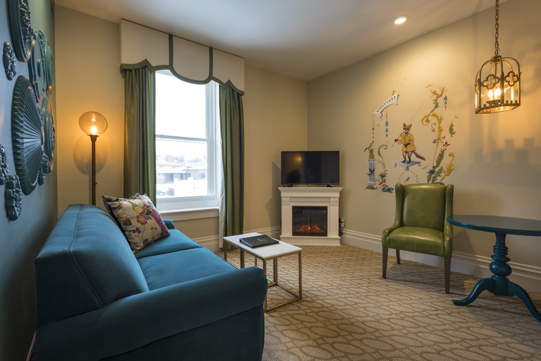 hotel king suite with white fire place, blue couch and green chair 