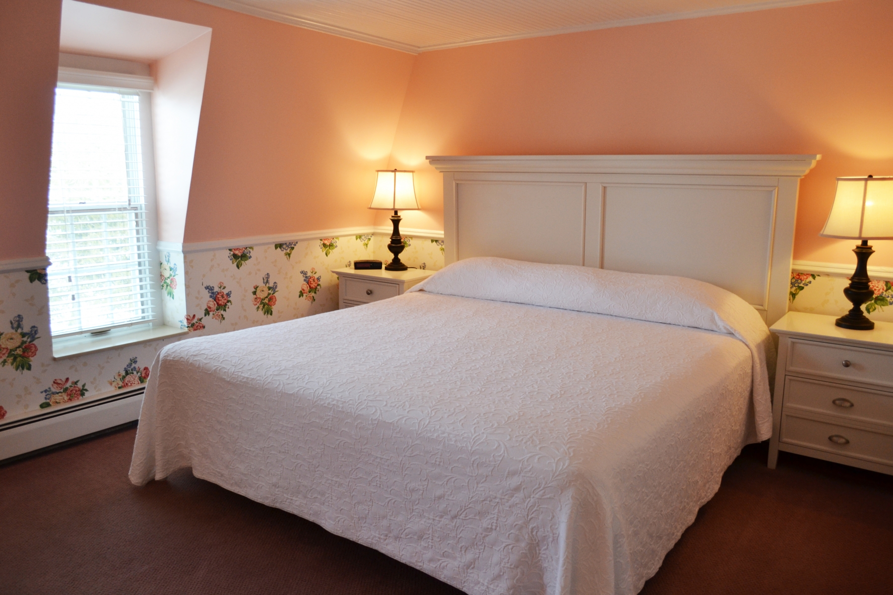 interior room with peach walls and floral wallpaper with a beautiful white king bed in the center of the room  