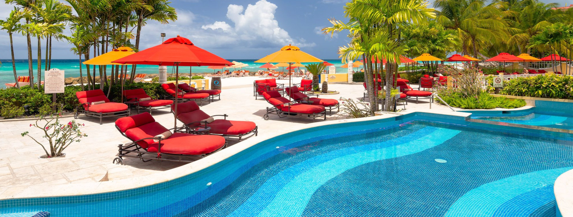 sun loungers around a swimming pool with the beach in the back