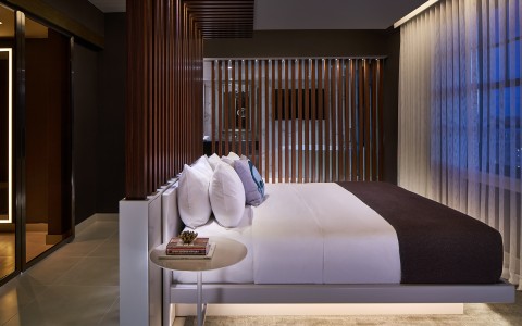 Side view of a bed facing the window and a modern wooden divider between the bedroom and the bathroom
