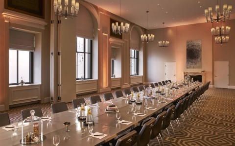 meeting venue with modern chandeliers and a long table in the middle of the room with glasses pens and paper