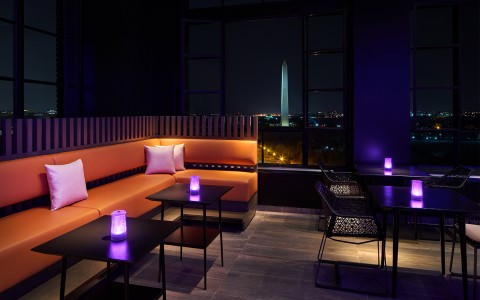 lounge area with orange corner couch and black tables with a window view of the national monument at night 