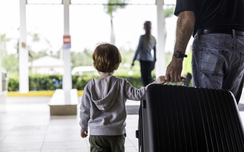 little boy and dad wheeling a large suitcase out of a hotel