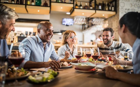 group of people laughing at table over food and drinks