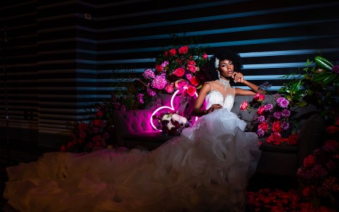 bride posing on couch with neon sign and flowers behind her