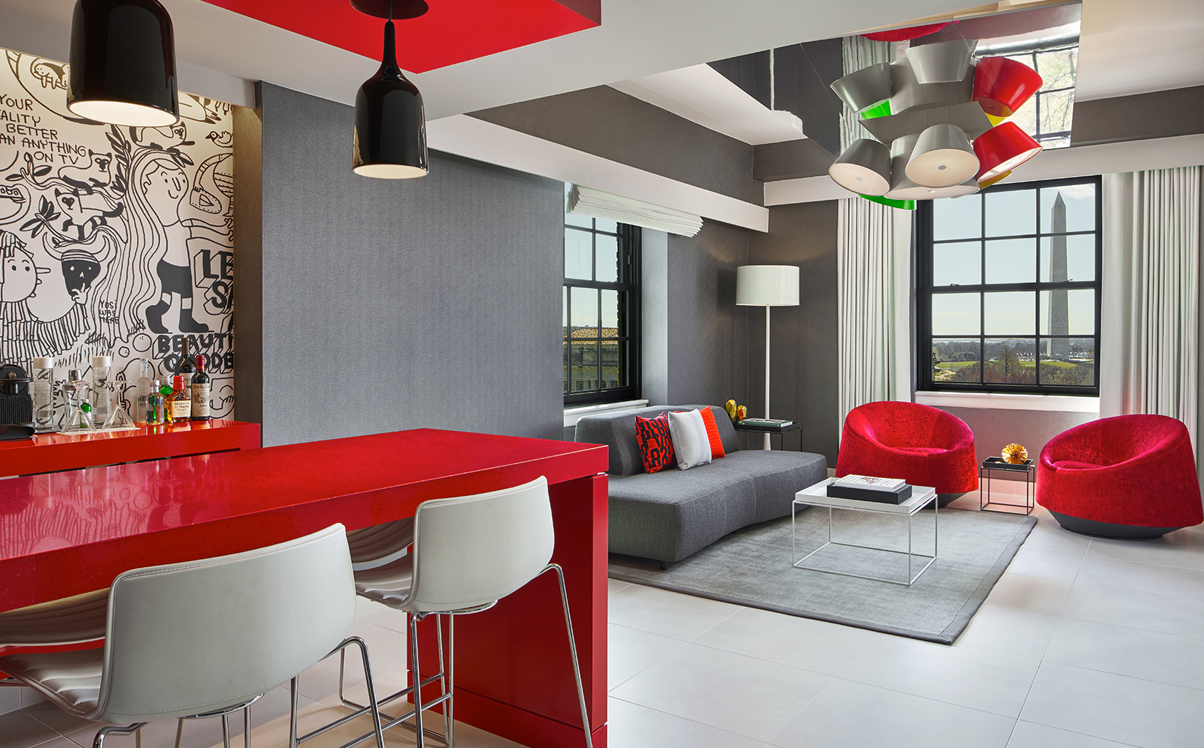Living area with red chairs and grey couches and red tables and white chairs in the dining area 
