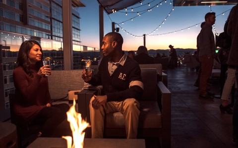 two guys next to the fireplace at the rooftop bar talking while they are holding their drinks