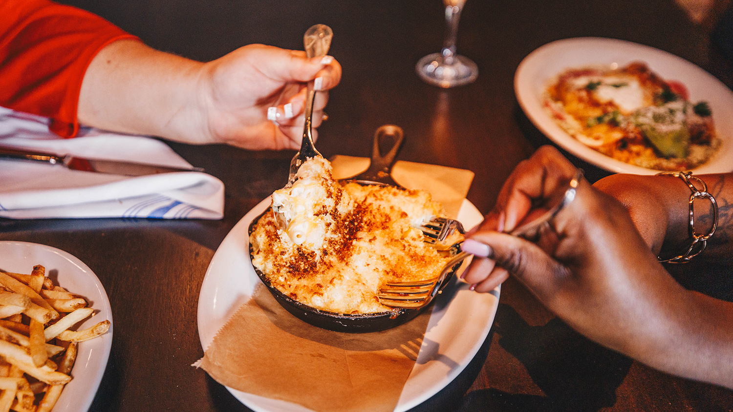 people digging a fork into mac n cheese in a skillet