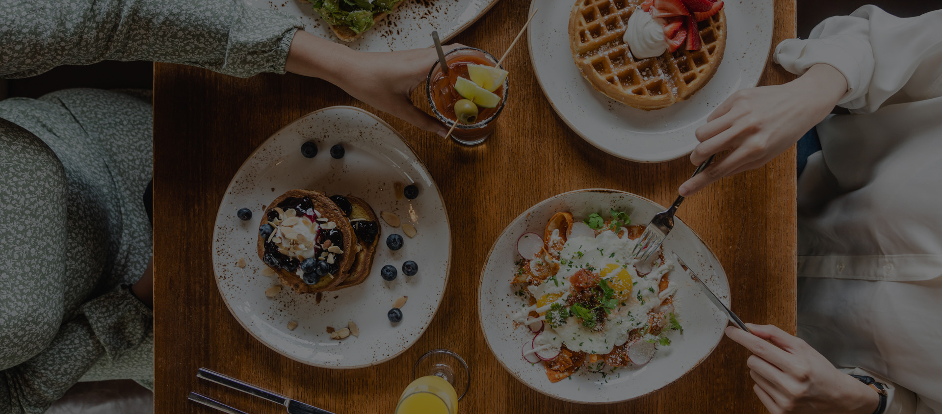 top view of breakfast plates on table and people cutting into the food
