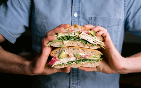 tasty giant ham and avocado sandwich and two hands holding it