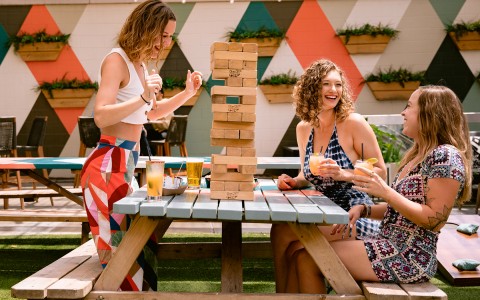 three girl friends playing Jenga while they are having some drinks at the pub