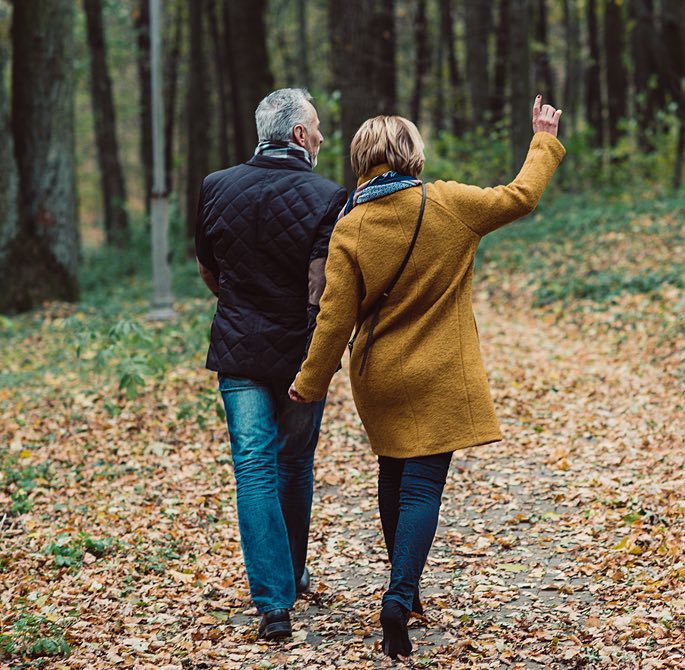 couple in winter clothes walking outside with leaves on the ground 