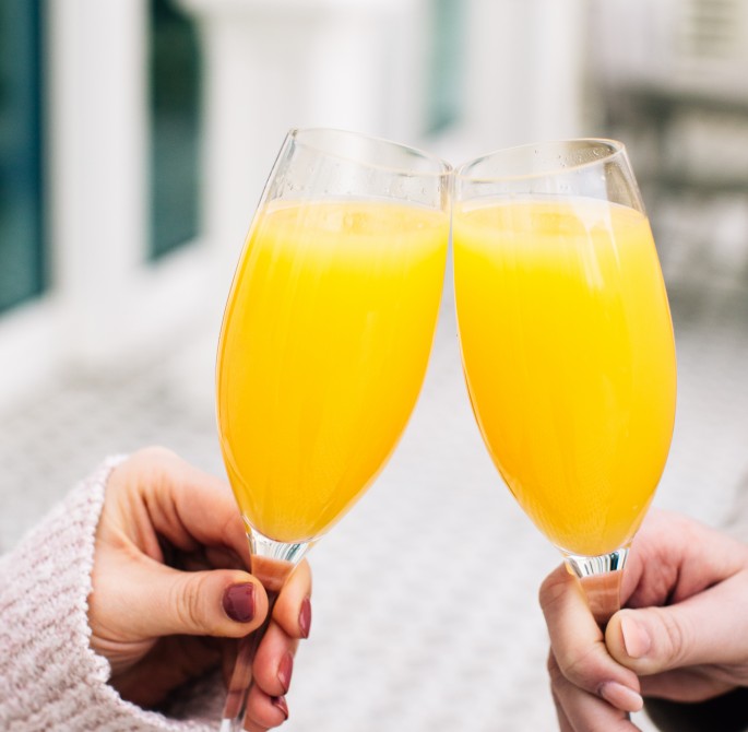 two people clinking mimosa glasses 