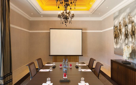 Meeting room with wooden table setup and projector screen on the wall