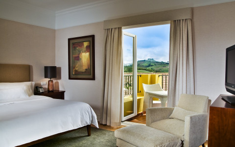 Guest room bed with white linens and white chair next to balcony