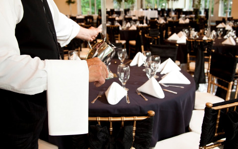 waiter pouring water to tables set up for an event with black tablecloths 