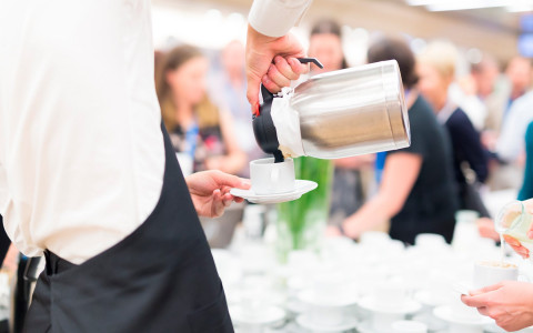waiter pouring coffee into a white cup 