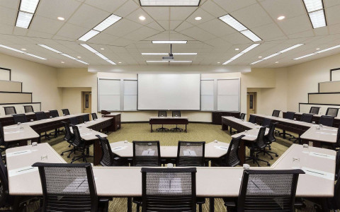 Two rows of octagonal desks surround a presenting desk and a large projector