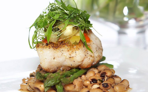 A elegantly plated fish sits over asparagus and beans