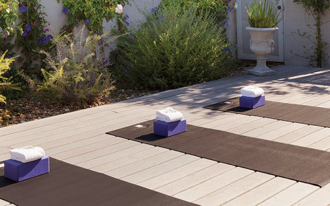 three yoga mats with folded towels on outside deck with bushes 