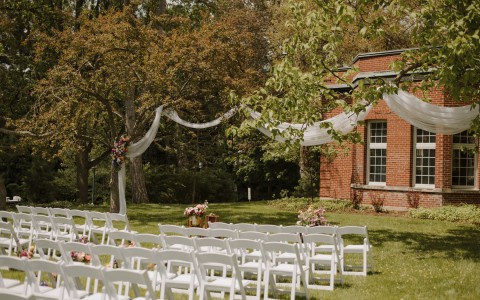a wedding ceremony set up on the exterior of the property with white chairs and white and pink flower decorations