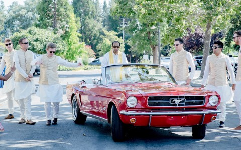 Indian wedding groom and groomsmen with a classic red car on their way to the ceremony