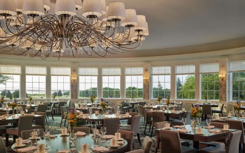 A large dining room with windows on all the walls looking out into the lawn of the hotel