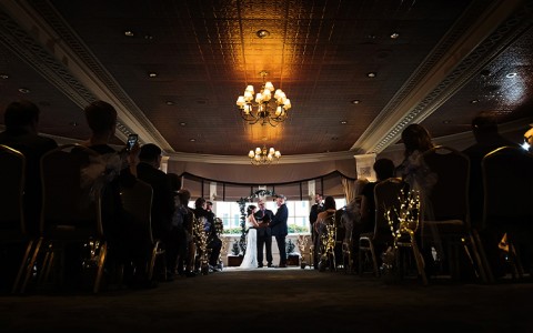 couple getting married indoors with a dim light above them, Photo Credits: Beau Ridge Photography